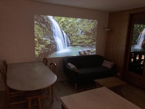 Ein Wohnzimmer mit Holztisch, dunkelgrauem Sofa und großem Fenster mit Blick auf einen Wasserfall.