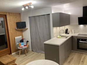Eine kompakte Küche mit Backofen, Spüle und einer kleinen Essecke mit einem Stuhl.