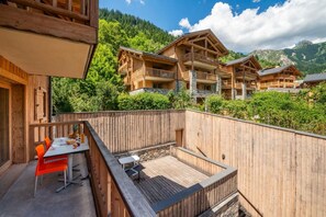 A wooden deck with a table and chairs, overlooking a mountainous landscape with multiple wooden buildings.