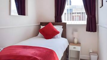A hotel room with a bed, a nightstand, a lamp, and a view of buildings through the window.