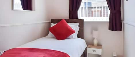 A hotel room with a bed, a nightstand, a lamp, and a view of buildings through the window.