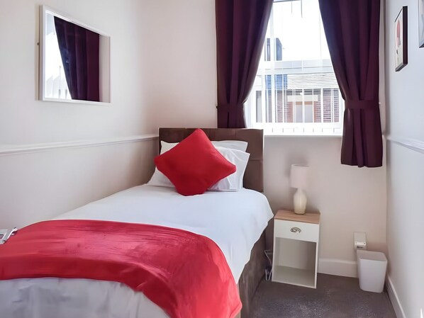 A hotel room with a bed, a nightstand, a lamp, and a view of buildings through the window.