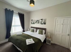 Een hotelkamer met een bed, nachtkastje, deur en kunst aan de muur.