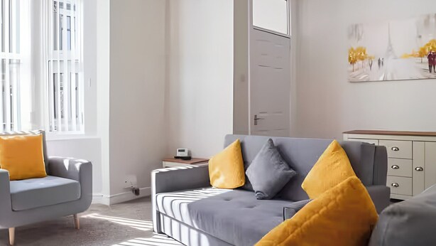 Ein modernes Wohnzimmer mit Sofa, Sesseln und Couchtisch. Eine Tür und ein Gemälde sind an der Wand zu sehen.