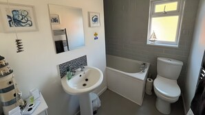 Ein Badezimmer mit einem weißen Waschbecken, einer Badewanne und einer Toilette. An den Wänden hängen Bilder in Rahmen und über der Toilette befindet sich ein Fenster.