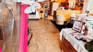 Ein gemütlicher, rustikaler Raum mit Holzwänden und einem Deckenventilator. Im Hintergrund ist eine Essecke mit einem Tisch für zwei Personen zu sehen.