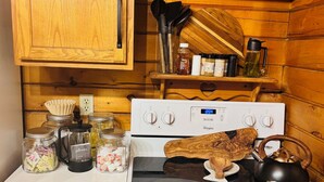 Uma cozinha com fogão branco, chaleira preta e diversos potes e recipientes na bancada.