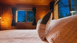 Um quarto aconchegante com teto de madeira, janela com cortinas e cama com colchão acolchoado e travesseiros.