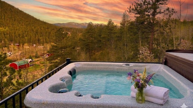 Banheira de hidromassagem com vista para a montanha, rodeada por árvores e um céu ao pôr do sol.