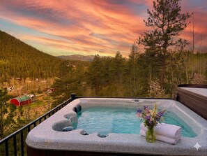 A hot tub with a mountain view, surrounded by trees and a sunset sky.