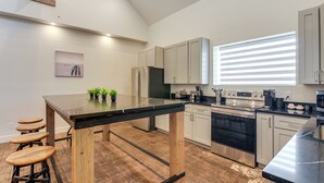 A modern kitchen with a black countertop, wooden stools, stainless steel appliances, and a large window with blinds. - Between Bryce Canyon & Zion: Hiker's Paradise! (Hatch)