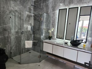 A modern bathroom with a glass-enclosed shower, a white sink with a black bowl, and a large mirror.
