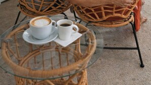 Two people sitting on wicker chairs facing a glass table with two cups of coffee. - Hotel VOS (Quepos)