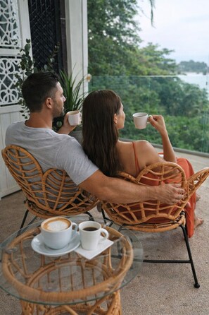 Two people sitting on wicker chairs facing a glass table with two cups of coffee. - Hotel VOS (Quepos)