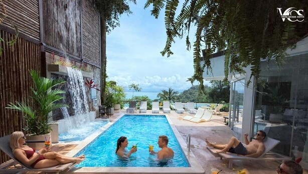 Uma área de piscina com cascata, espreguiçadeiras e vista para o oceano.