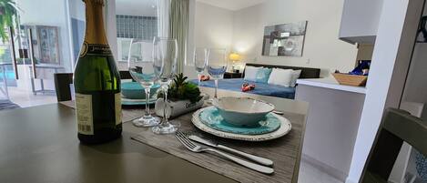 A dining table set with a bottle of champagne, glasses, and plates, in a modern living room with a sofa and artwork.