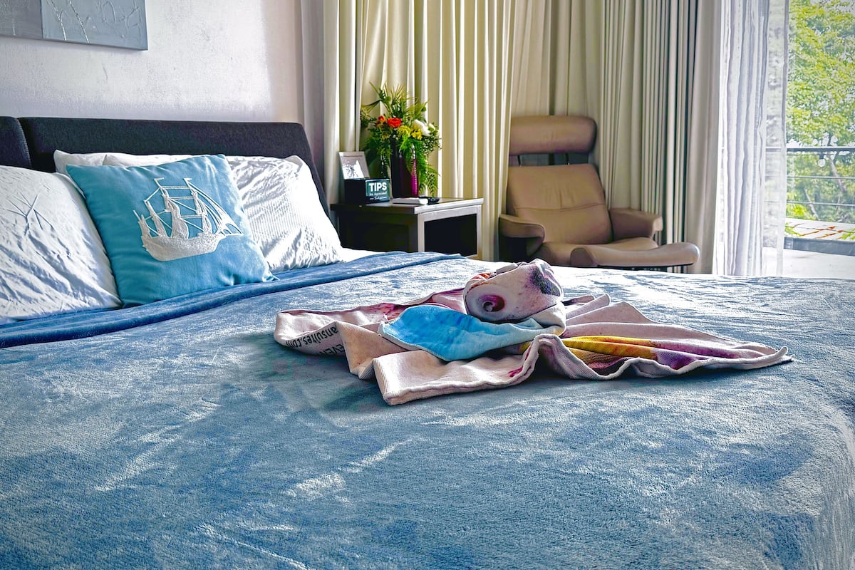 A hotel room with a bed, a chair, a nightstand, and a window with curtains.