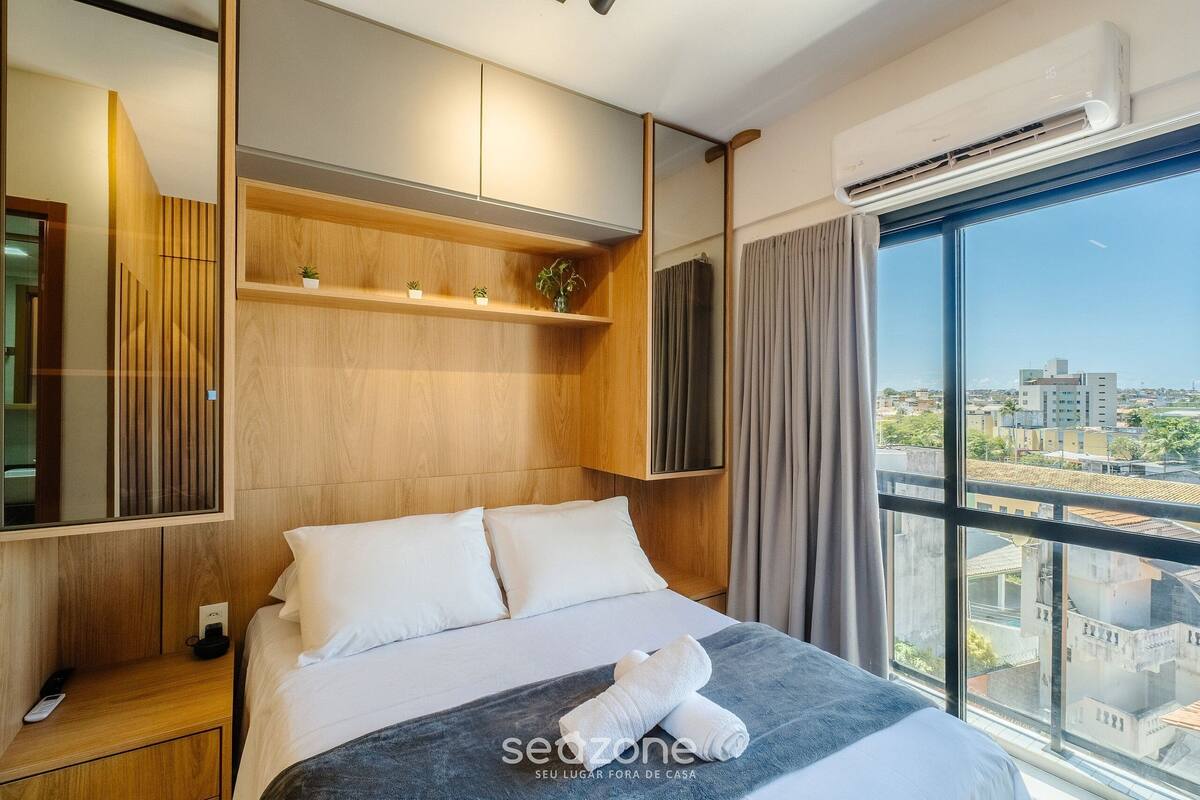 Une chambre d’hôtel moderne avec un grand lit, des panneaux de bois, un téléviseur fixé au mur et une vue sur la ville.