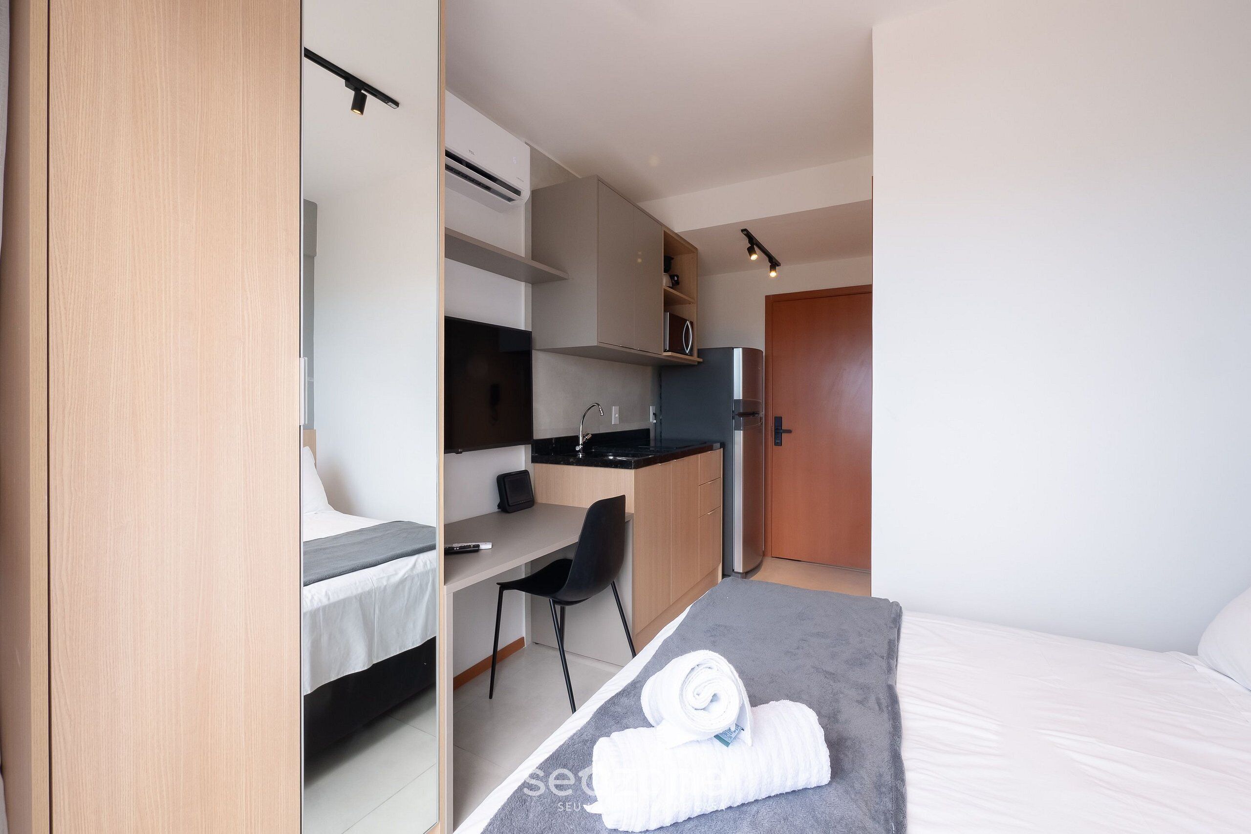 A modern hotel room with a bed, a desk, a chair, a kitchenette, and a bathroom.