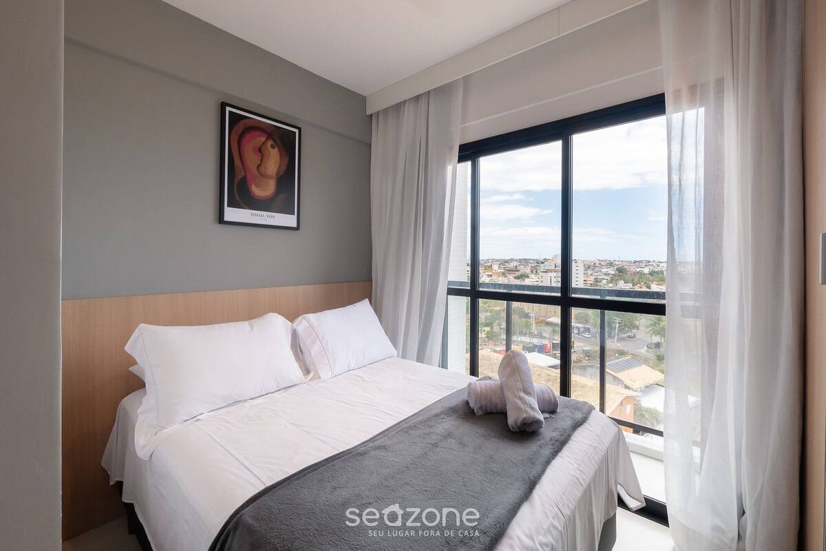 Une chambre d’hôtel moderne avec un grand lit, une vue sur la ville et une œuvre d’art encadrée au mur.