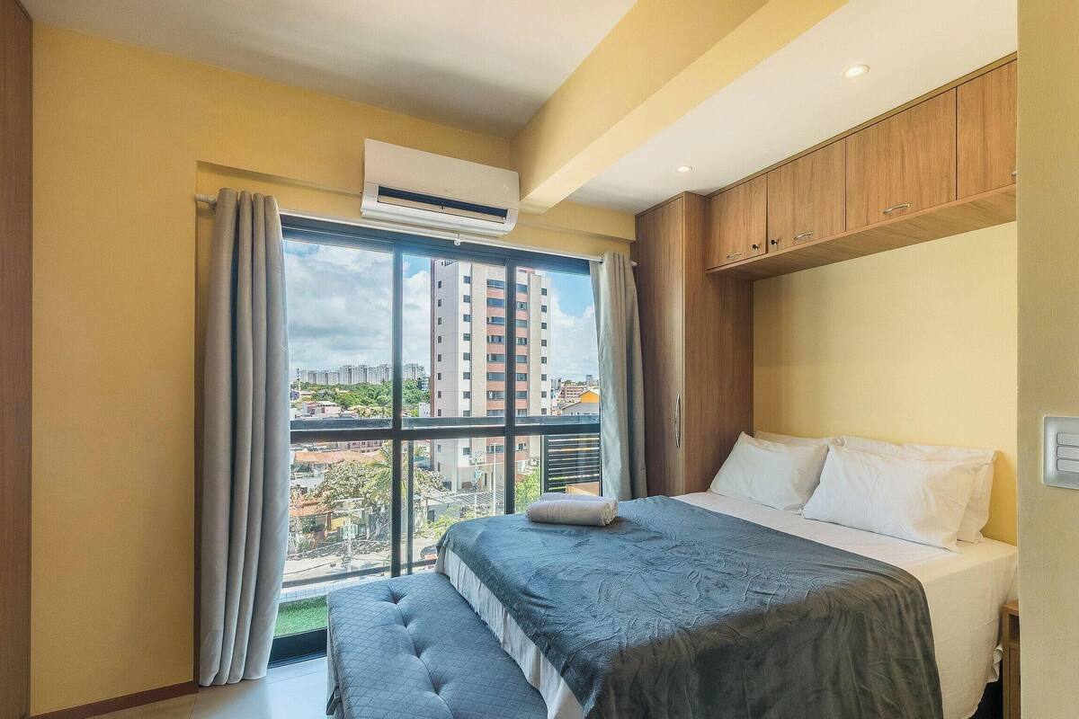 Une chambre d’hôtel avec un grand lit, une fenêtre avec des rideaux, un appareil de climatisation et une vue sur les bâtiments environnants.