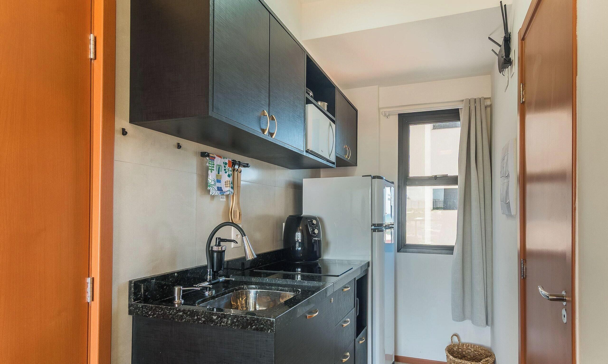 Una cocina compacta con armarios oscuros, un lavamanos de acero inoxidable y una cafetera.