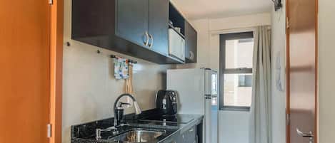 Una cocina compacta con armarios oscuros, un lavamanos de acero inoxidable y una cafetera.
