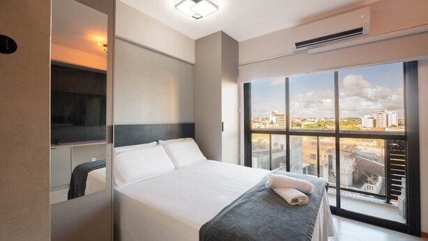 Una habitación de hotel moderna con una cama grande, una mesita de noche, un espejo y una ventana con vistas a la ciudad.