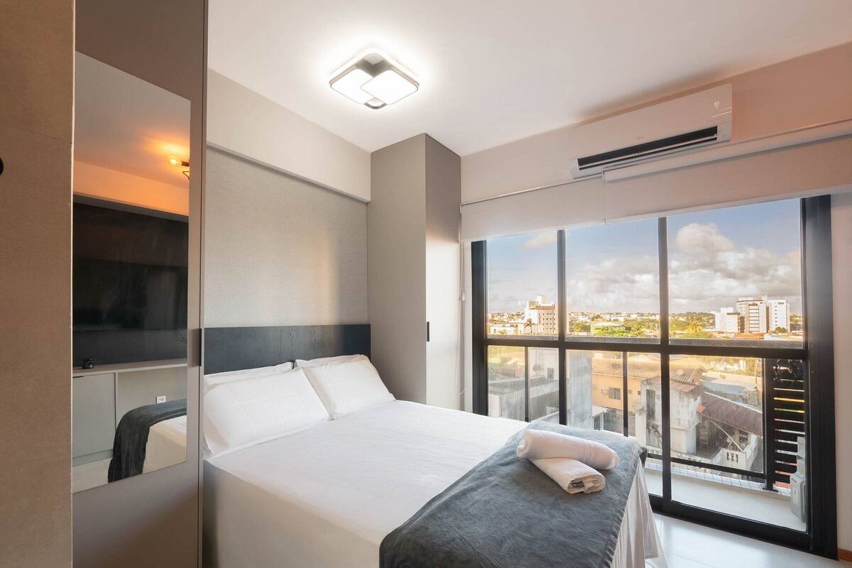 Une chambre d’hôtel moderne avec un grand lit, une table de chevet, un miroir et une fenêtre donnant sur la ville.
