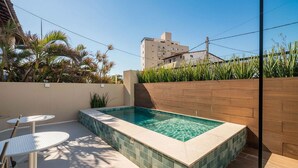 Una piscina rectangular con bordes de azulejos, rodeada por un muro de ladrillo bajo y palmeras.