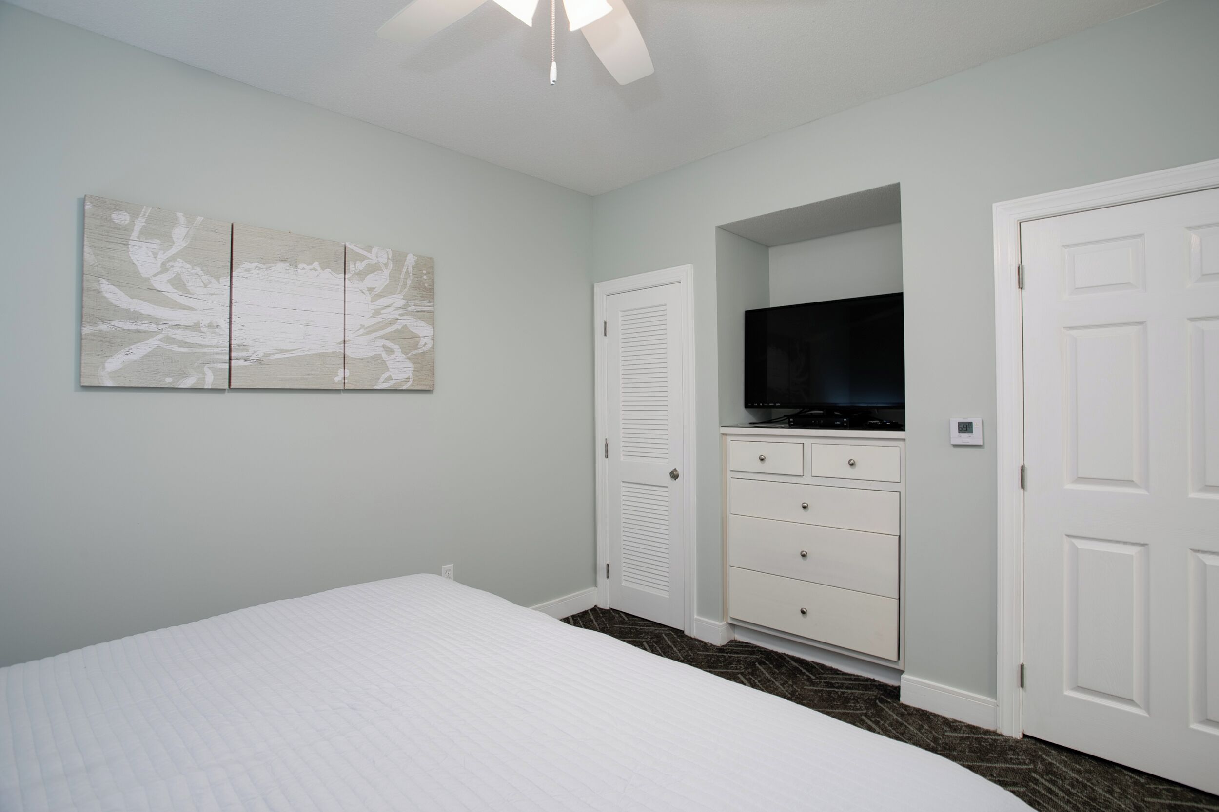 A bedroom with a bed, a dresser, a television, and a wall-mounted artwork.