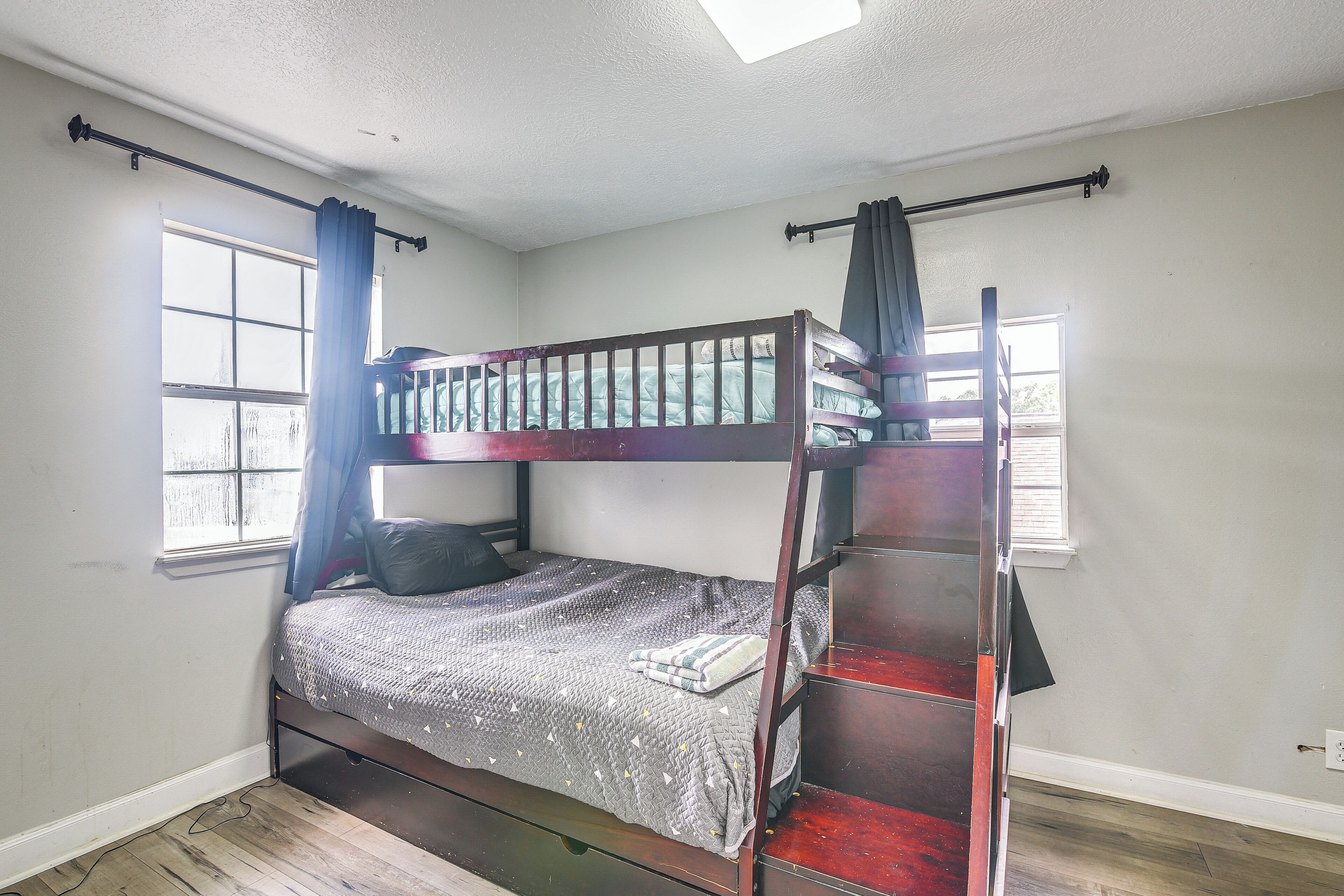A bunk bed room with a window, curtains, and a wooden floor.