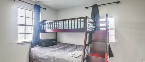 A bunk bed room with a window, curtains, and a wooden floor.