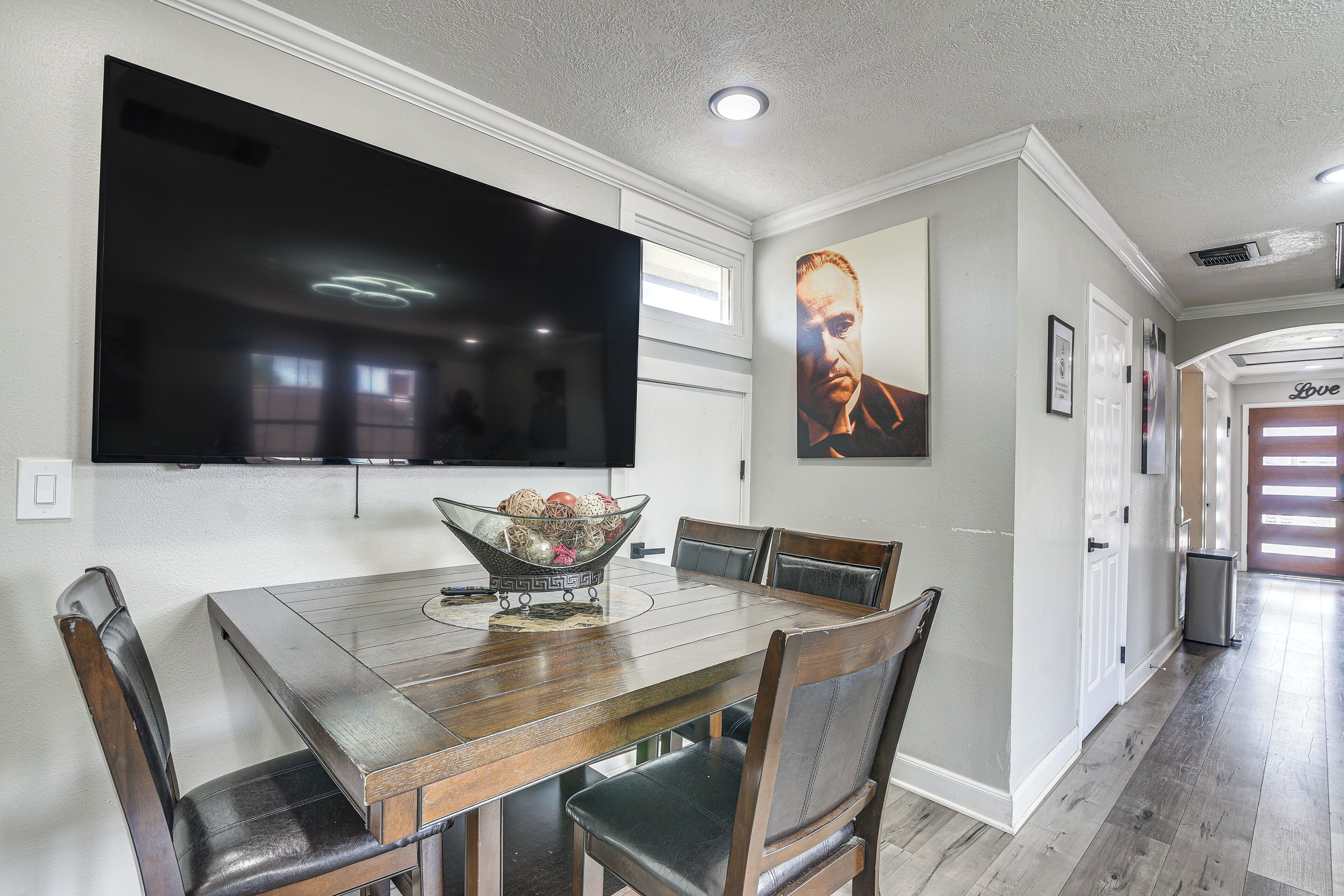 A dining area with a wooden table, chairs, a large flat-screen TV, and a wall-mounted picture.