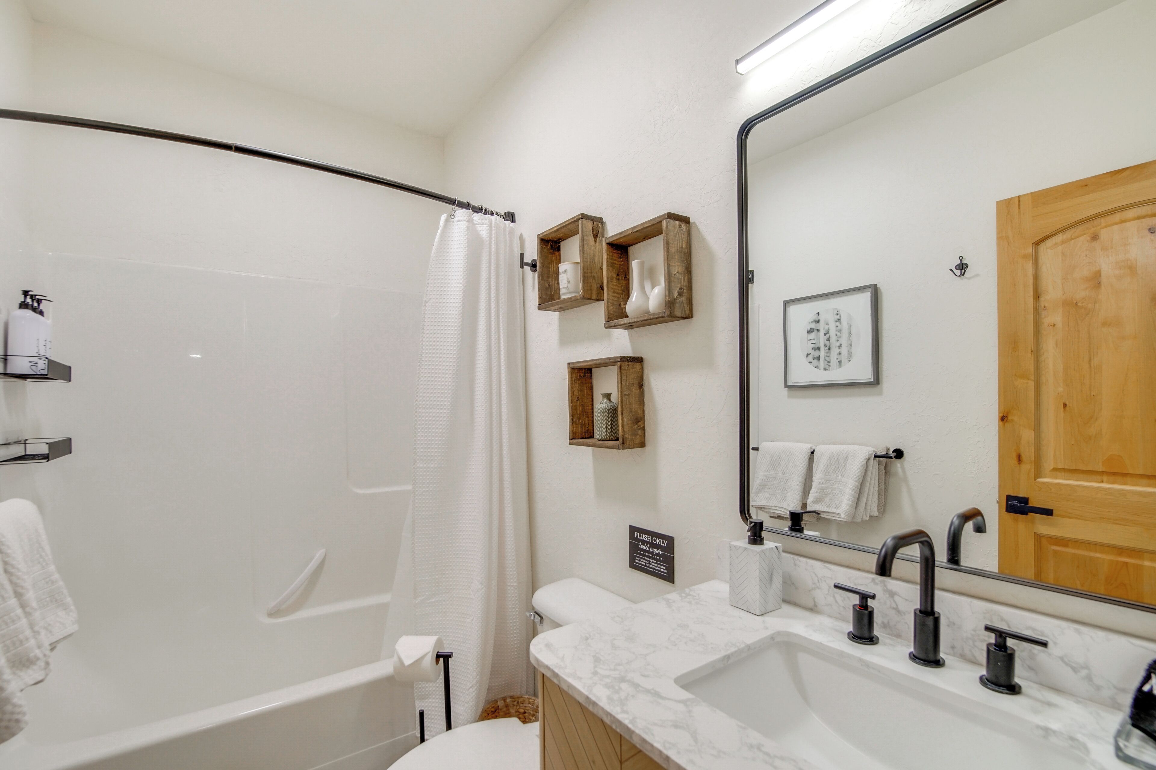 A modern bathroom with a bathtub, a sink with a mirror, and wooden shelves.