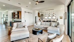 A spacious living room with a large sofa set, a coffee table, and a dining area with a kitchen in the background. - Luxury Beachfront Living! Epic Ocean Springs Home (Ocean Springs)