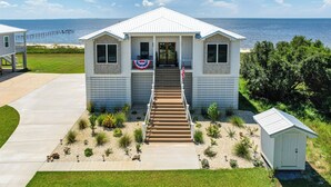 A small, single-story house with a front porch, a flag, and a view of the ocean. - Luxury Beachfront Living! Epic Ocean Springs Home (Ocean Springs)