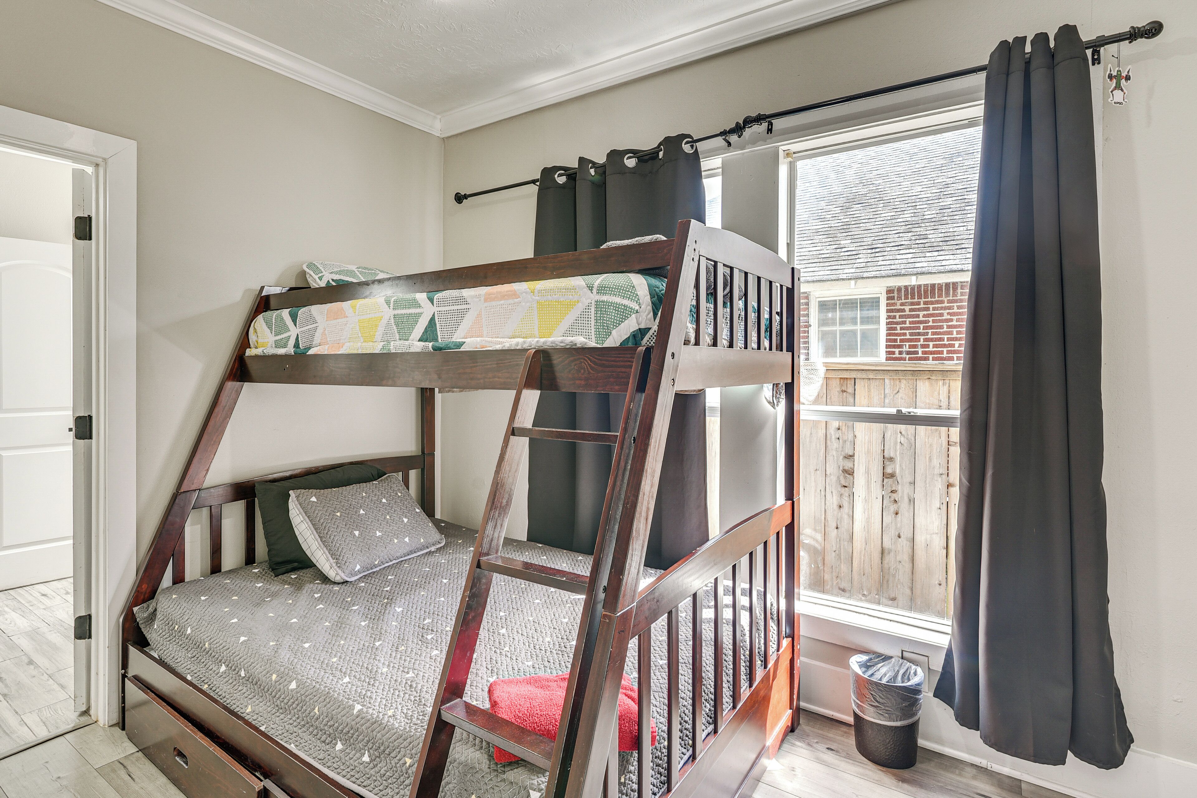 A bunk bed with a ladder, a window with curtains, and a door.
