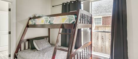 A bunk bed with a ladder, a window with curtains, and a door.