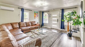 Een ruime woonkamer met een bruine leren hoekbank, een glazen salontafel en een potplant.