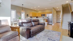 A spacious living room with a leather sofa, a dining area with a white table, and a kitchen with wooden cabinets and stainless steel appliances. - < Half-Mi to Lake: Townhome w/ Hot Tub in McHenry! (McHenry)