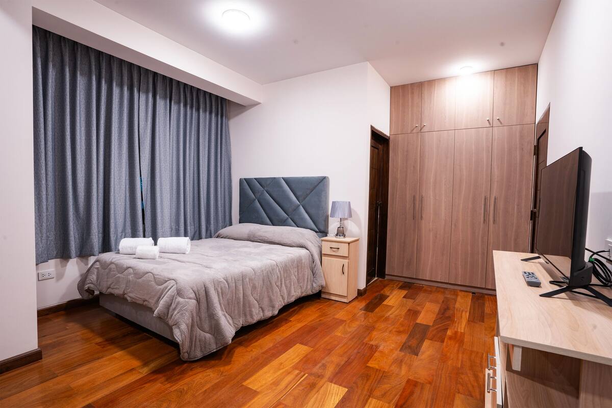 Un dormitorio moderno con cama, mesita de noche, televisor y armario.
