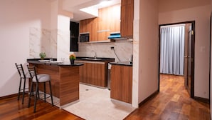 Una cocina moderna con armarios de madera, salpicadero de mármol y una pequeña isla con taburetes de bar.
