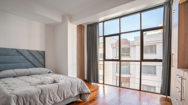 Un dormitorio con cama, un ventanal grande y suelo de madera.