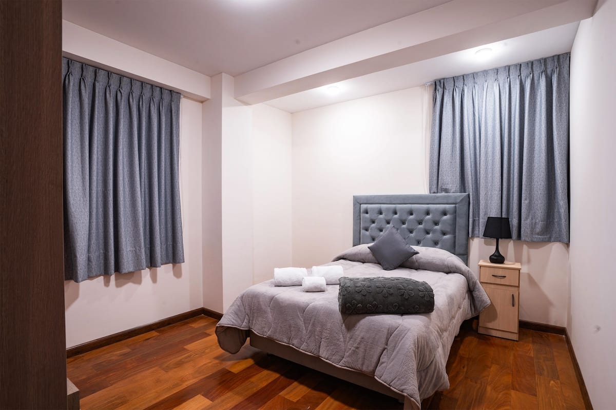 Un dormitorio con cama, mesita de noche y cortinas.