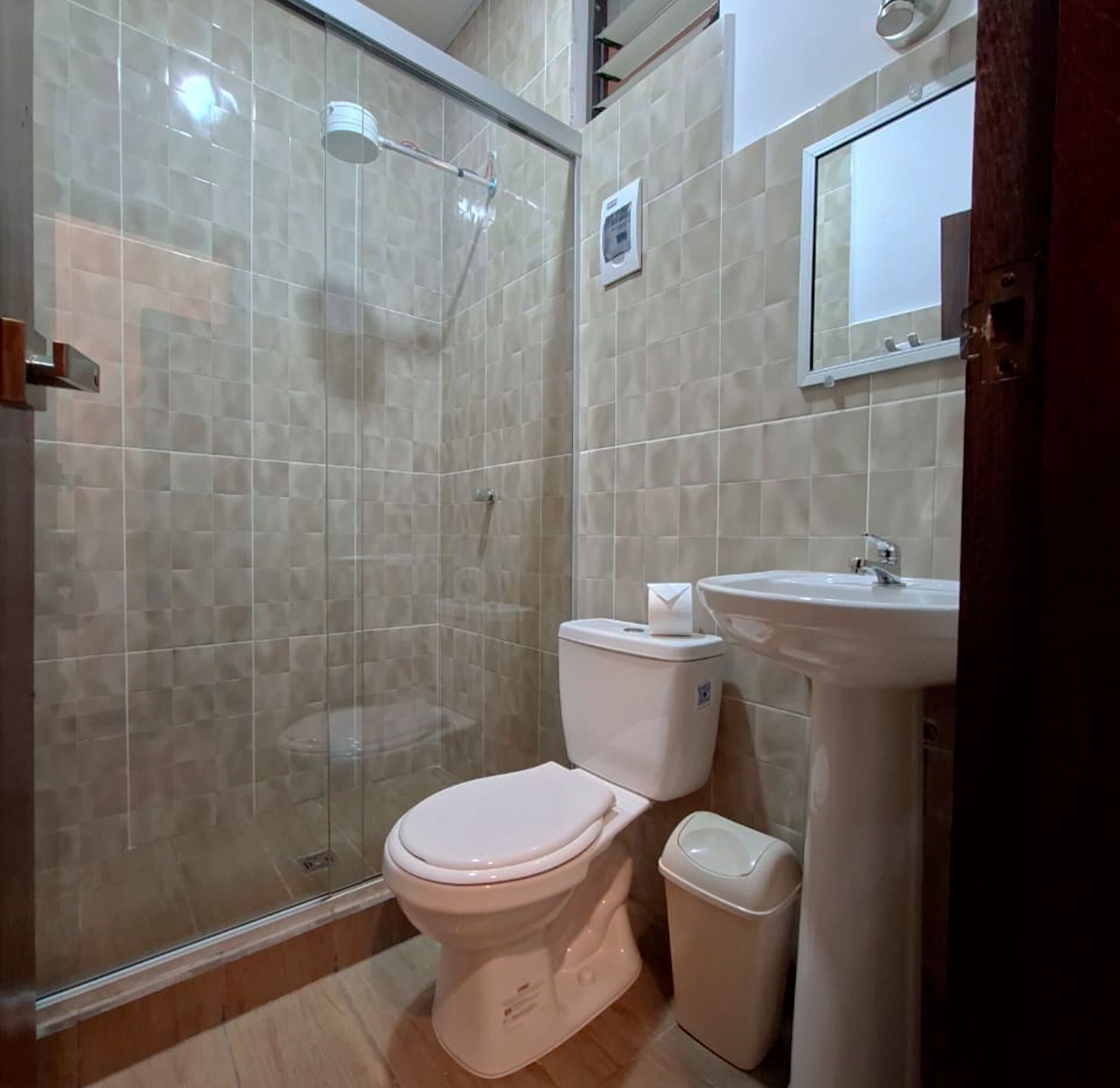 Un baño con ducha de vidrio, inodoro, lavamanos y un cesto de basura.