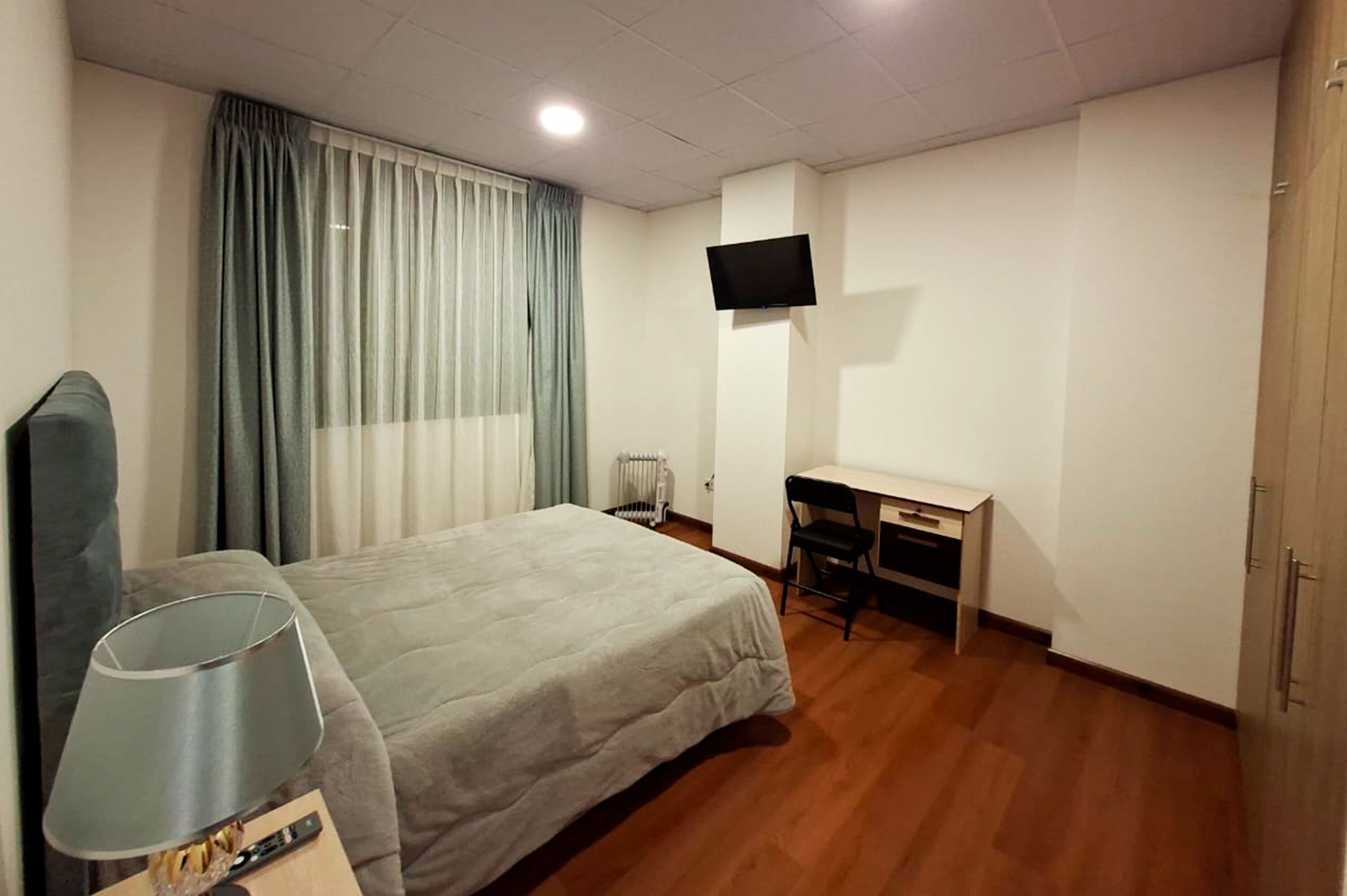 A hotel room with a bed, a desk, a chair, a TV, and a lamp.