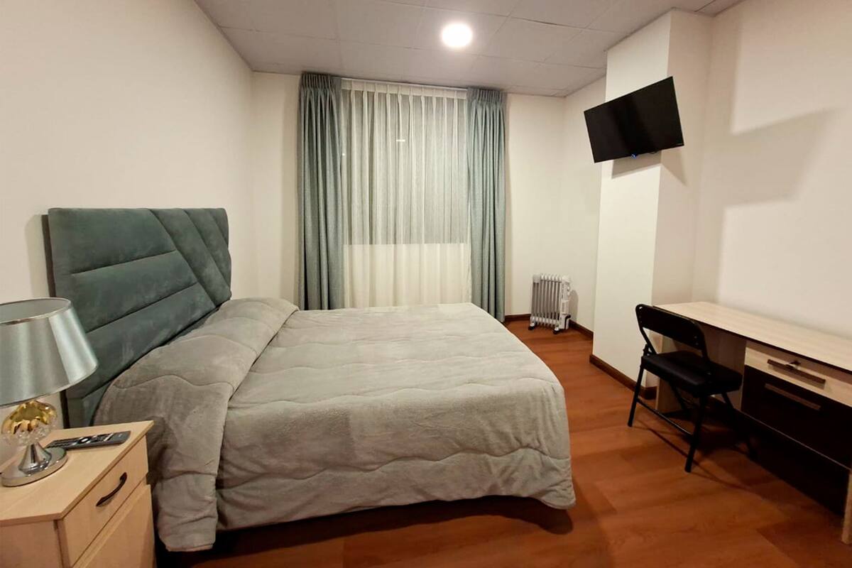 Un dormitorio con cama, mesita de noche, lámpara, televisión y un escritorio con silla.