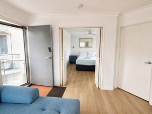 A room with a bed, a small bedside table, a mirror, and a door leading to another room.