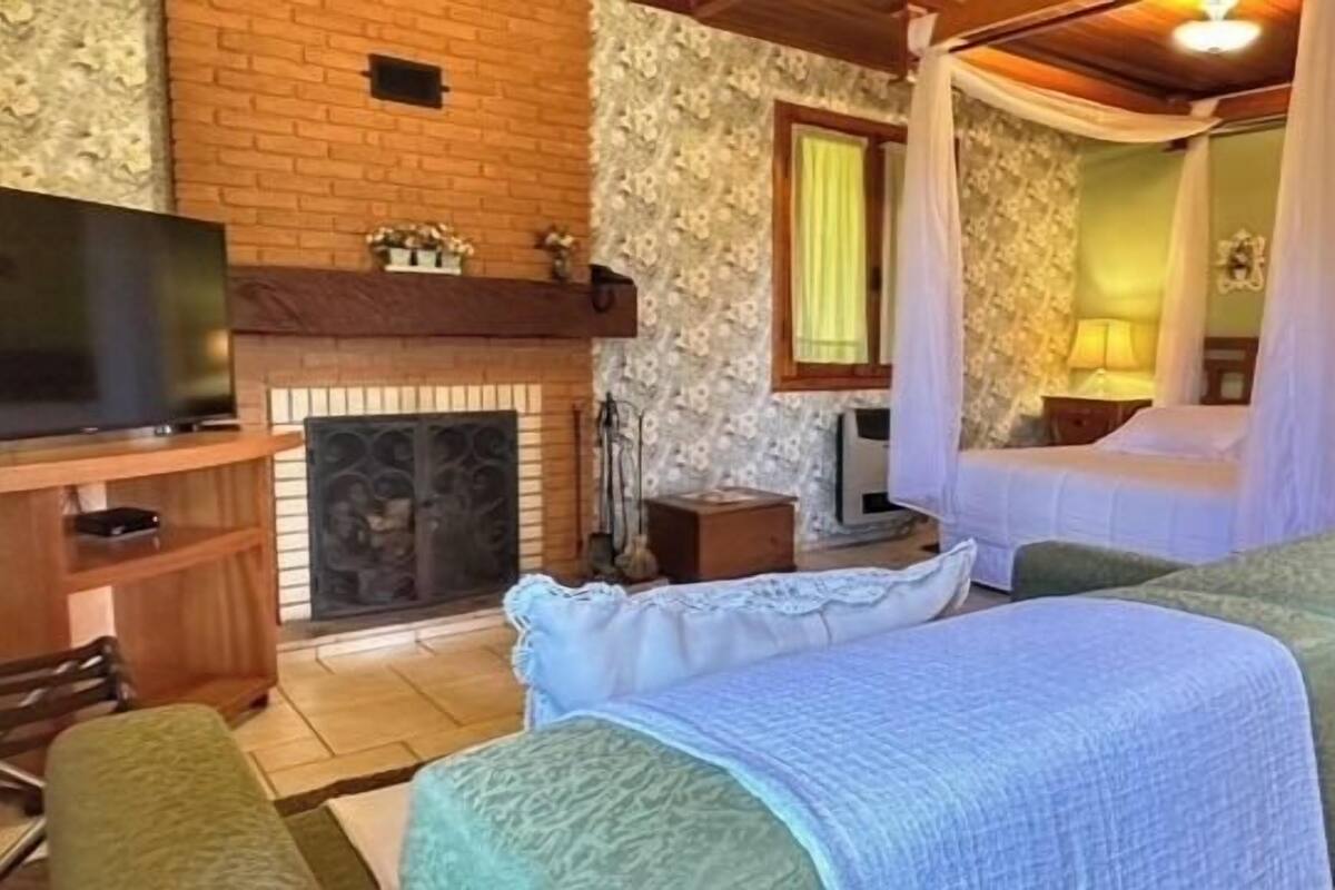 Un dormitorio con pared de ladrillo, televisión, chimenea, cama con dosel y sofá verde.